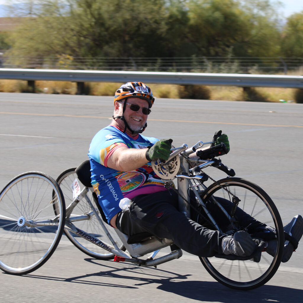 A man smiles while riding an adaptive bicycle