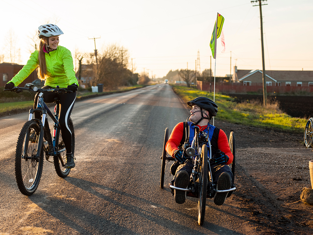 Woman riding bike and disabled man riding handcycle on country road