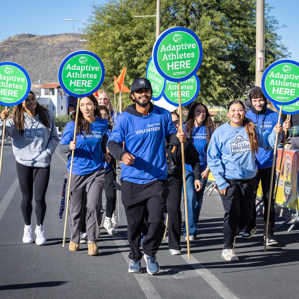 Volunteers walk at El Tour Tuscon while holding signs that read Adaptive Athletes here