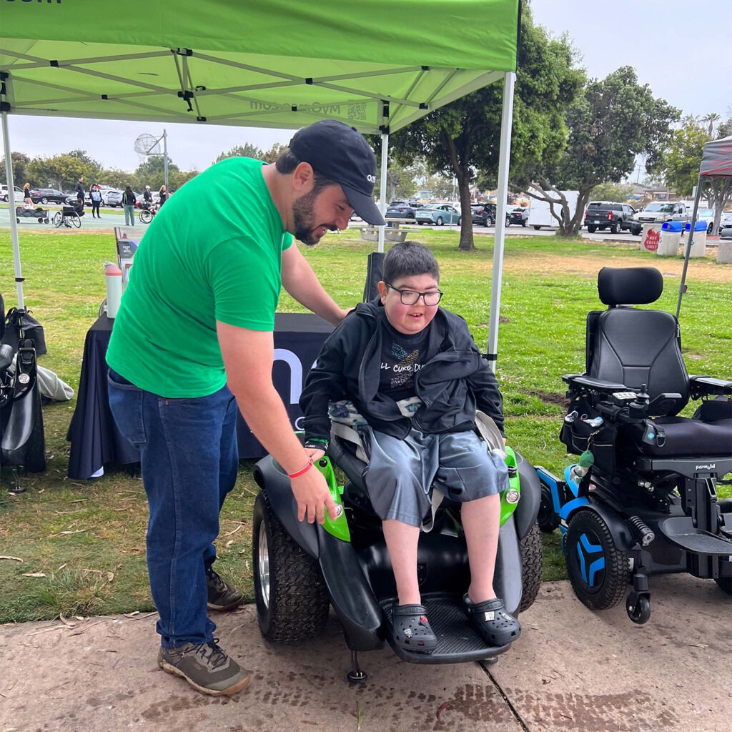A young man sits in an Omeo while a volunteer assists