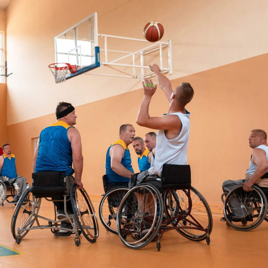 Disabled War veterans mixed race and age basketball teams in wheelchairs playing a training match in a sports gym hall.