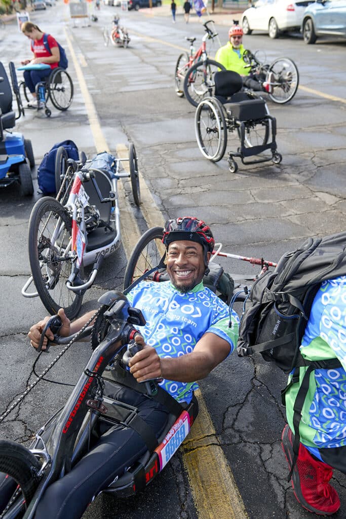 Adaptive cyclist prepares for El Tour de Tucson while seated on a handcycle in the rider staging area.