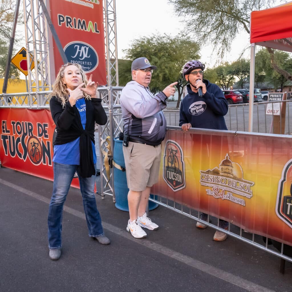 Event organizers and an American Sign Language (ASL) interpreter provide announcements and accessible communication before El Tour de Tucson.